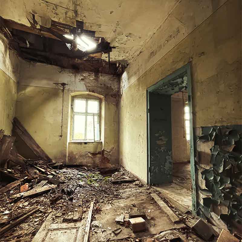 ads an abandoned room with a collapsed ceiling, debris on the floor, peeling walls, and a blue door with chipping paint.