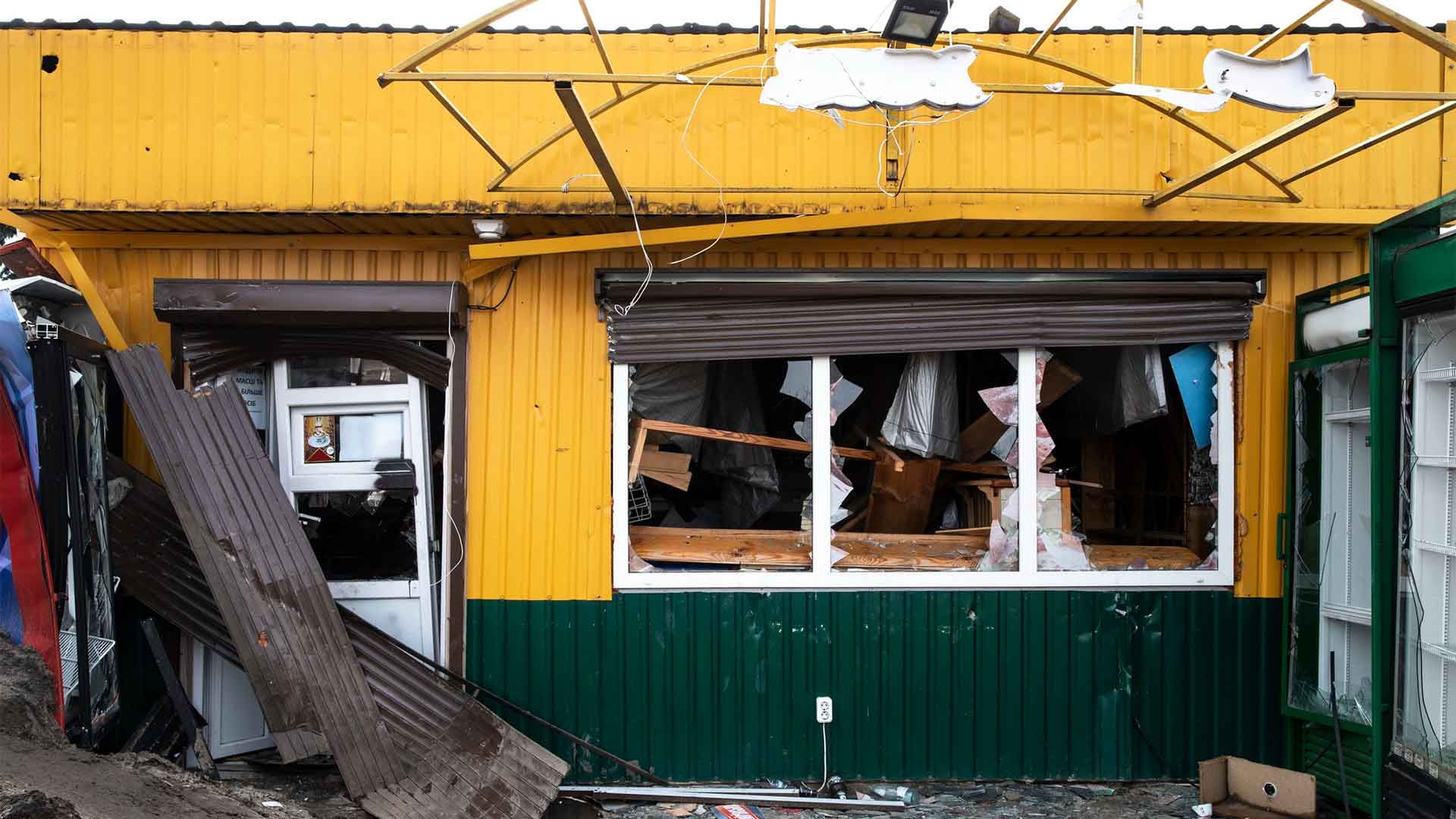 destroyed-house-russian-s-war-ukraine abandoned yellow building with a green base. The damaged corrugated metal roof and walls, broken windows, and scattered debris add to the eerie atmosphere.